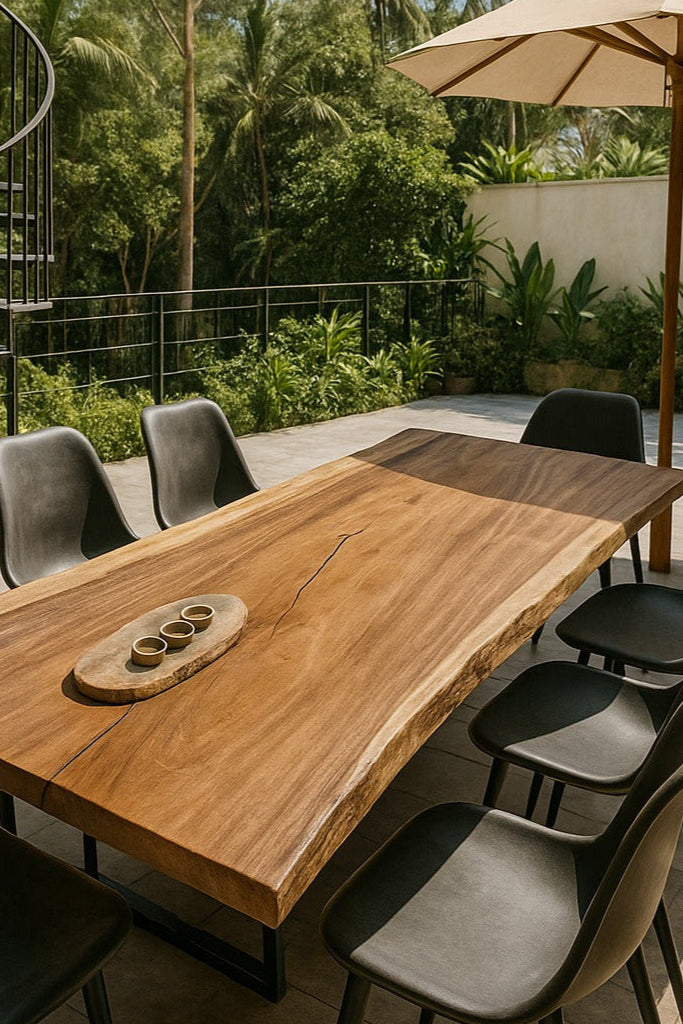 Outdoor dining area with wooden table and chairs under a large umbrella, surrounded by greenery.