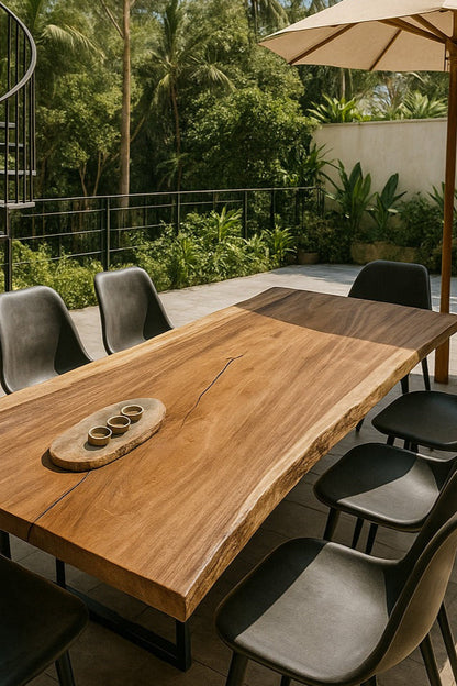 Outdoor dining area with wooden table and chairs under a large umbrella, surrounded by greenery.
